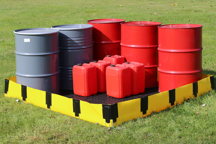 Oil drums and jerry cans on a spill containment barrier in a grassy area