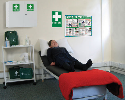 Child lying on a first aid couch with first aid supplies and posters in the background.