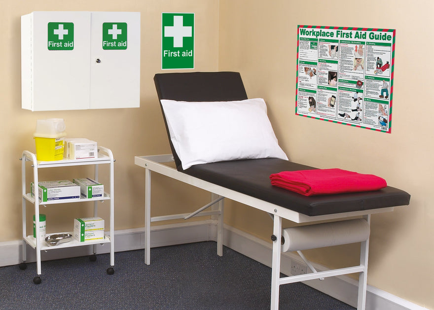 First aid station with a treatment table, shelves, and first aid guide on the wall.