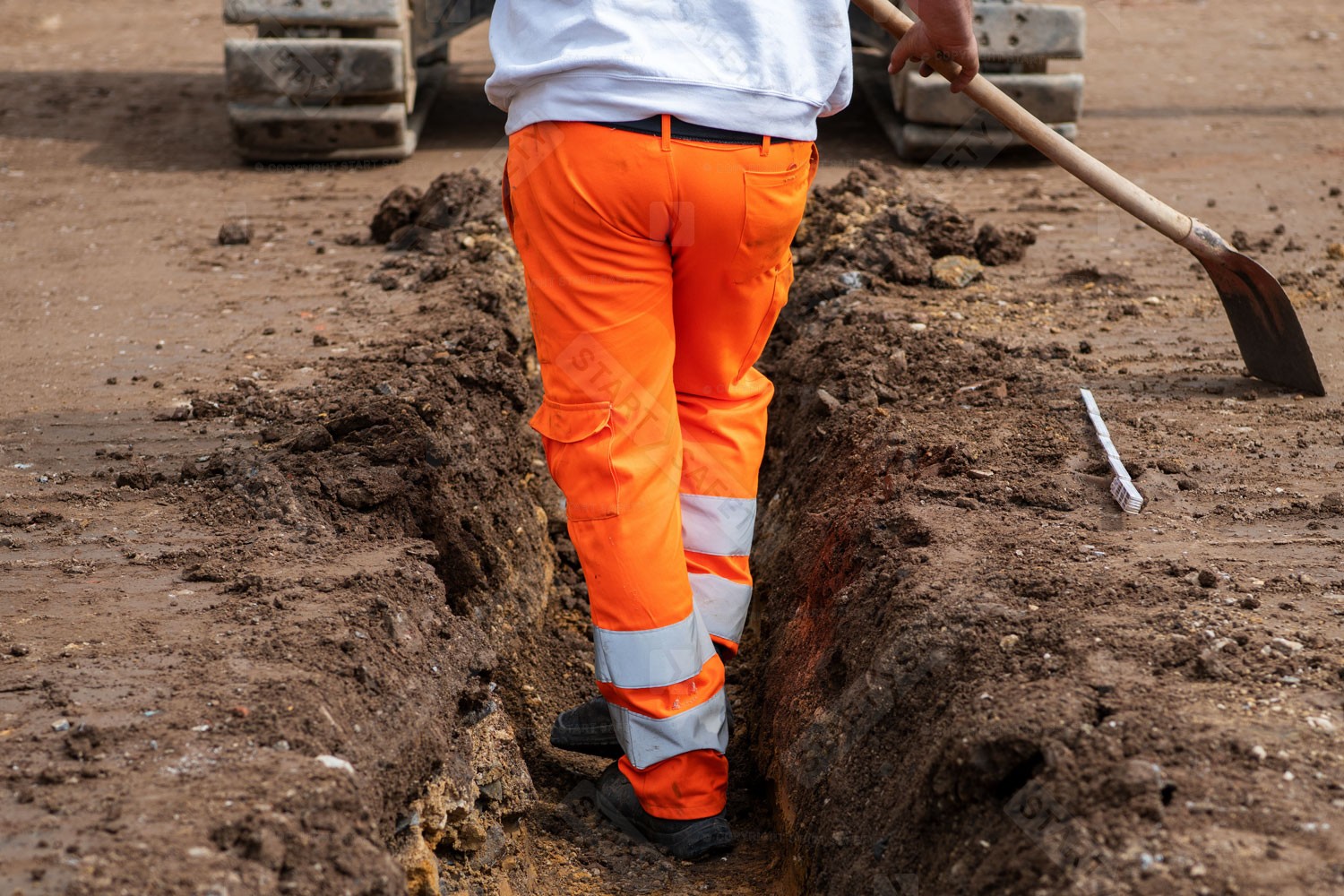 Worker Weating Orange Hi Vis Waterproof Trousers On Construction Site