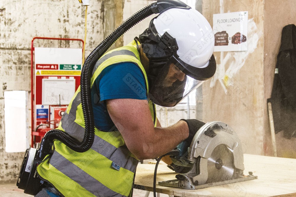 Worker Cutting Plywood While Wearing A Powered Air Mask