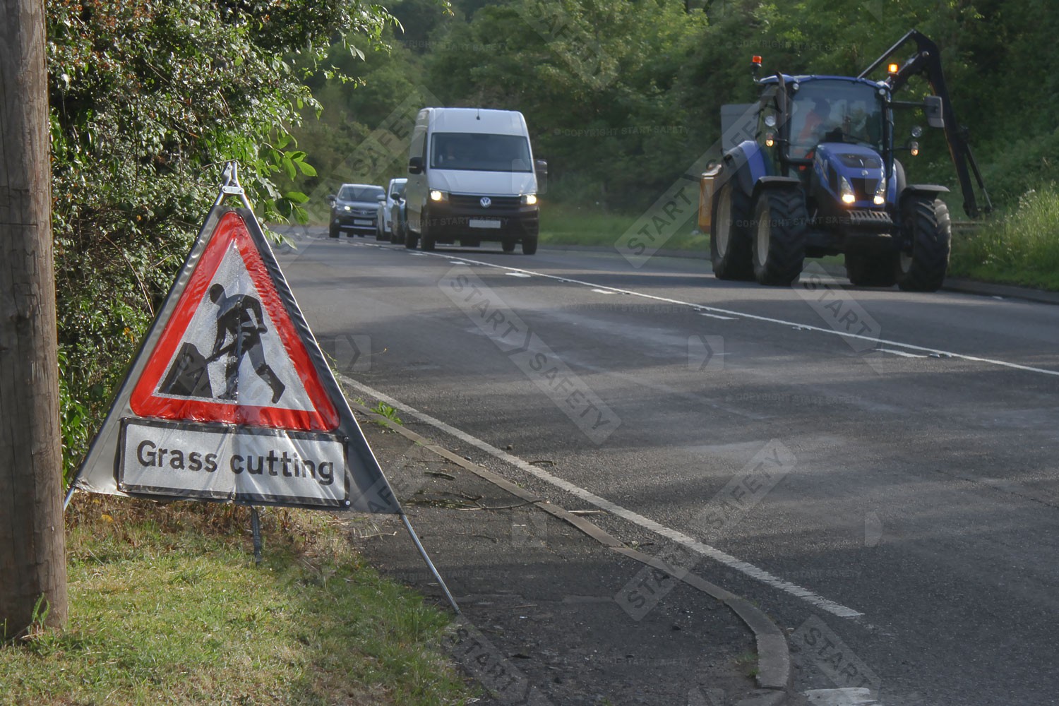 Men At Work Grass Cutting Folding Sign In Use On The Side Of A Busy Main Road